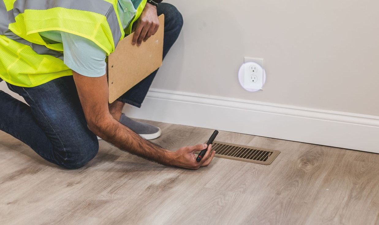 A construction worker in a hard hat inspects a floor vent indoors, ensuring quality and safety standards.